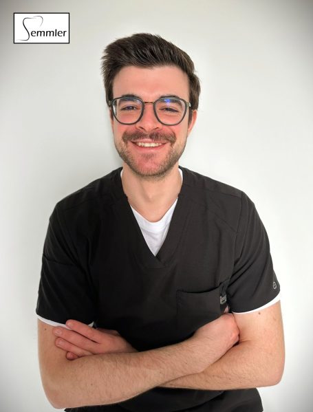 Mann in schwarzer Arbeitskleidung mit Brille und lächelndem Gesicht. Arme verschränkt.